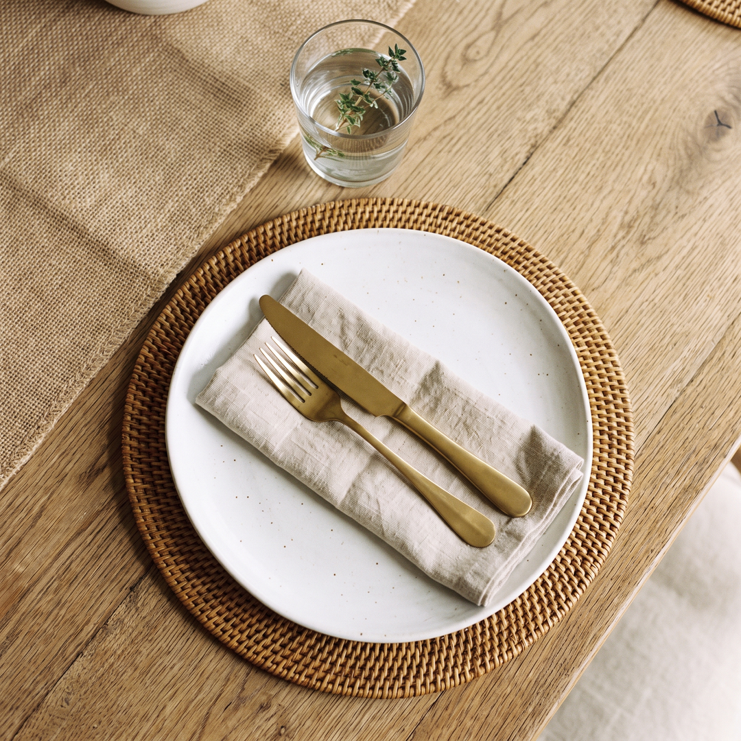 Couvert dressé sur un set de table rond en rotin, assiette blanche et serviette en lin